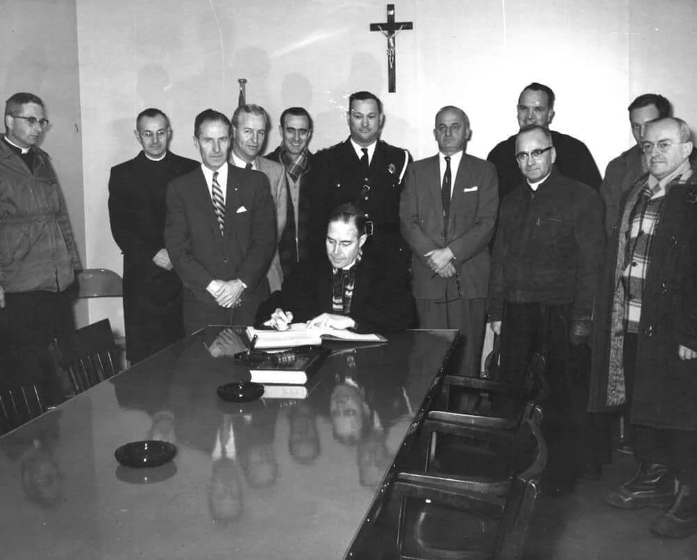 Mons. Couturier y los visitantes reunidos alrededor de una mesa